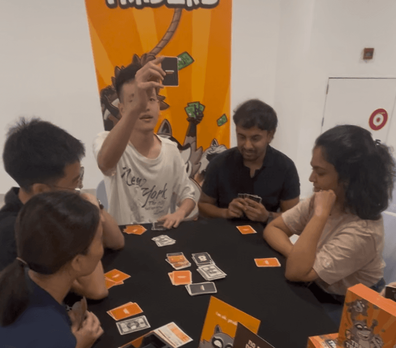 Players around a Trash Traders table, one holding a card up
